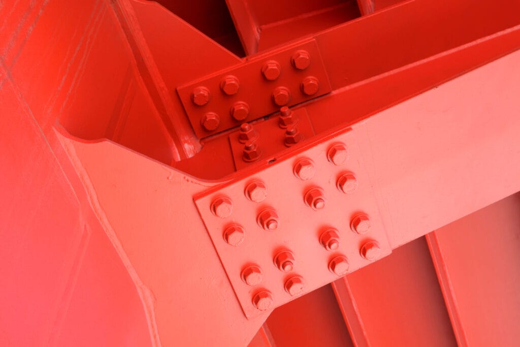 The red iron beam is bolted down. Close-up shows the connection of the steel powerful straight crossbar, bridge connection, metal architecture.